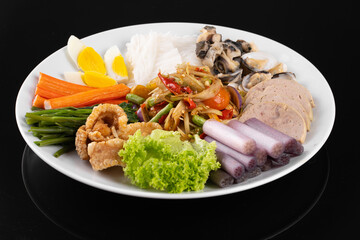 Colorful dish with assorted fresh vegetables, boiled eggs, squid, and noodles served on a white plate, displayed on a black background.