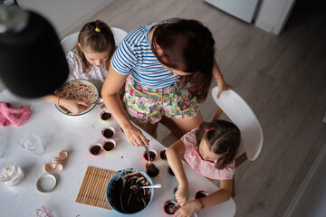 Top view of a mother and her two daughters making cupcakes in the kitchen, illustrating family bonding, cooking and creating together in a joyful home environment.