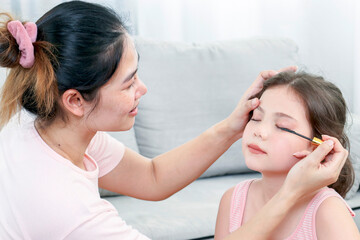 Young Asia mother and little daughter are doing make up for each other and having fun. Family spend time together have a fun in living room with happy holiday concept,happy family.