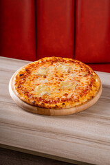 Delicious cheese pizza on a wooden platter in a cozy restaurant setting with red booth seating in the background.