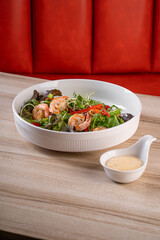 Delicious fresh shrimp salad with arugula, cherry tomatoes, and dressing served on a wooden table with a bright red background.