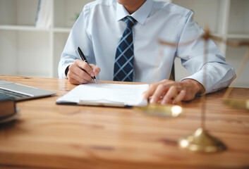A lawyer in a suit is sitting at his desk, signing legal documents with a gavel on the side.