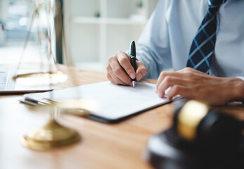 A lawyer in a suit is sitting at his desk, signing legal documents with a gavel on the side.