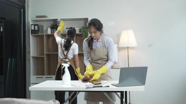 Two women contractors working as housekeepers in an office, wiping glass, sweeping floors, mopping, and cleaning sofas. Providing full-service cleaning for homes, condos, factories, and hotels