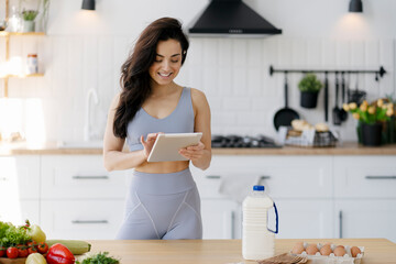 Young woman checking online recipe on tablet while preparing healthy meal in kitchen