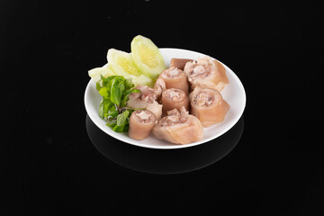 Delicious pork trotters with lettuce, beautifully plated on a white dish against a black background, perfect Asian cuisine photo.