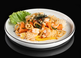 Delicious seafood pasta dish with shrimp and vegetables served on a white plate, garnished with fresh lettuce on a black background.