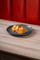 Delicious serving of spaghetti pasta topped with seafood in a stylish black plate against a modern red background.