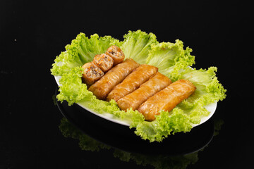 Delicious spring rolls served on a bed of fresh green lettuce, presented on a white plate against a black background.