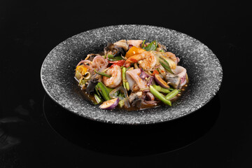 Delicious stir-fried seafood with mixed vegetables served on a granite plate on a black background.