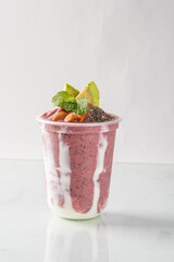 Delicious strawberry smoothie with fresh fruit toppings in a clear cup on a white background.
