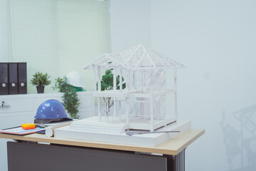 A home design company's office with a house sample placed on a desk, showcasing house structure design and drafting plans. The scene focuses on architecture, with no people present.