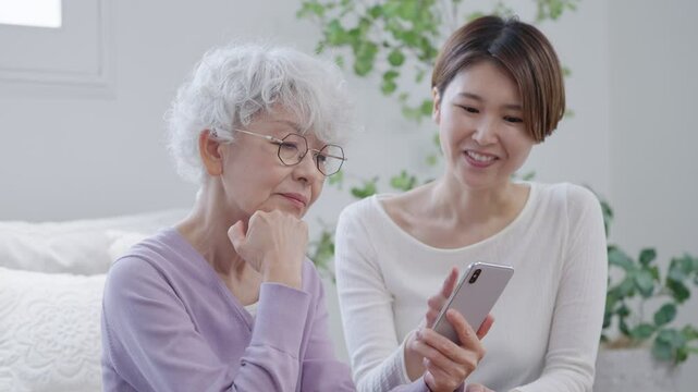 高齢者の母親にスマホを教える娘（家族・ファミリー）
