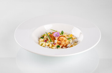 Elegant gourmet dish with grilled scallop, vegetable garnish, and flowers served in a white bowl on a clean, white background.