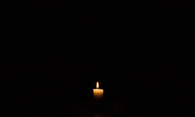 A dimly lit room with all lights turned off featuring a single candle flickering softly on a wooden table