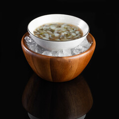 Elegant presentation of a white bowl with a tasty soup, placed in a wooden bowl filled with ice...