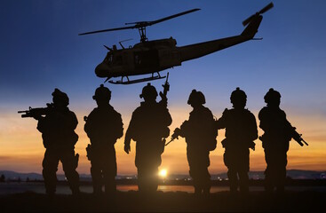 silhouette of military special force unit with helicopter in the background under sunset sky