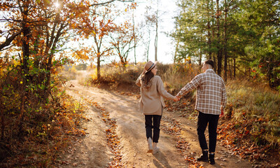 Obraz premium A couple enjoys a joyful moment together on a serene autumn day in a colorful forest setting with vibrant foliage and soft sunlight. The concept of youth, love and lifestyle.
