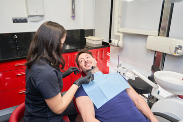 A woman helps a man get his teeth cleaned. The man is smiling, the woman is wearing gloves.