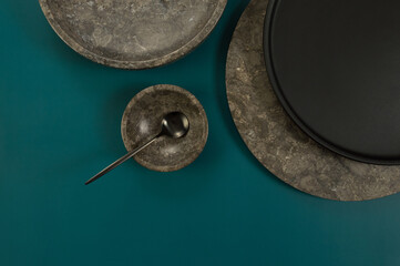 Top view of brown marble tray, bowl, black plate and cutlery on dark green background. Food presentation, dishes, stone tray. Copy space, flat lay.