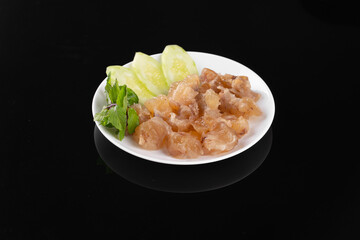 Plate of cooked chicken cartilage garnished with fresh lettuce and parsley on a black background for culinary presentation.