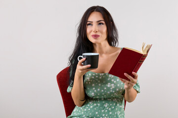 Naklejka premium portrait of a beautiful woman with long hair holding a mug and reading a book.
