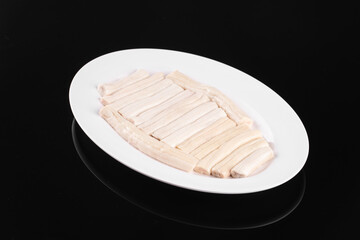 Raw razor clams neatly arranged on a white plate against a black background, ready for cooking or preparation.