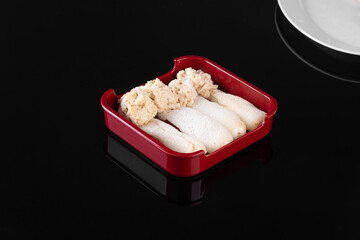 Red tray with fresh squid slices and garnish, placed on a black surface with a partial view of a...