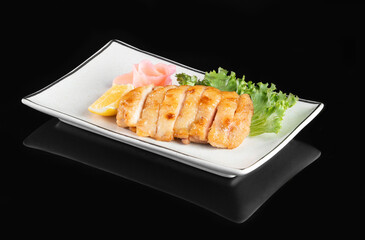 Sliced grilled chicken breast served on a white plate with garnish of greens and lemon on a black background.