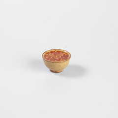 Small bowl of spicy chili sauce on plain white background, ideal for culinary or food-related projects.