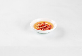 Small white bowl of hot broth with sliced red chili peppers on white background, minimalistic spicy food concept.