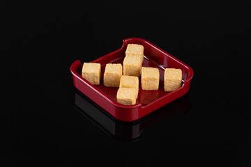 Square tofu cubes served in a minimalist red plate on a reflective black background, showcasing a simple and elegant food presentation.