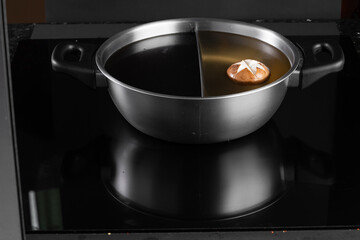 Stainless steel hot pot with a divider, filled with broth and a mushroom, placed on an induction...