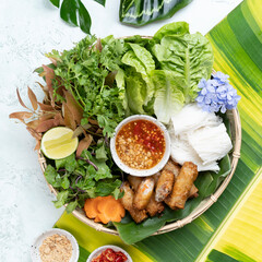 Top view of a vibrant, fresh Vietnamese salad with various greens, herbs, spring rolls, and dipping sauces, beautifully arranged on a plate.