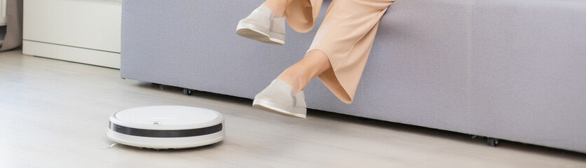 Young woman using automatic vacuum cleaner to clean the floor, controling machine housework robot