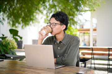 Young asian man thinking while looking to his laptop. Man working on his laptop at the outdoor cafe in the morning