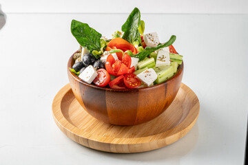 Fresh and colorful Greek salad with tomatoes, cucumbers, olives, feta cheese, and spinach in a wooden bowl on a wooden plate.