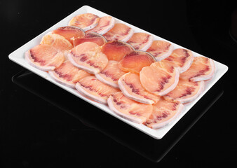 Fresh, thinly sliced pieces of raw fish arranged neatly on a white rectangular plate, displayed on a black background.