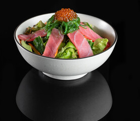 Fresh tuna sashimi salad with seaweed and fish roe in a white bowl on black background. Perfect for food blogs and culinary content.
