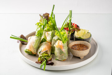 Fresh Vietnamese spring rolls with shrimp, herbs, and dipping sauce, beautifully served on a white plate against a clean background.