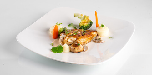 Gourmet dish of grilled fish filet with vegetables and creamy sauce elegantly presented on a white plate.