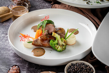 Gourmet dish with vegetables and steak, beautifully plated with sauces, served on a white plate in a restaurant setting.