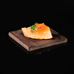 Gourmet salmon sushi on a wooden plank with elegant presentation against a black background, highlighting its fresh ingredients and delicacy.