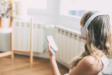 Close up of a blonde woman listening to music with headphones holding smartphone