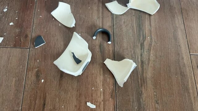Broken ceramic cup on dark wooden floor. Top view