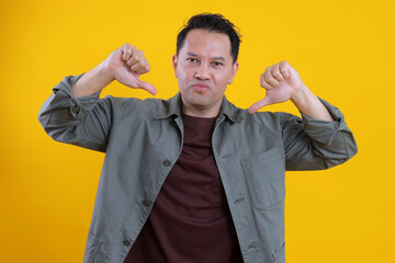 Asian Young Man Showing Two Thumbs Down Isolated on Yellow Background