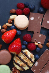 Macarons, chocolate, cookies, berries and various nuts on dark blue background. Top view.