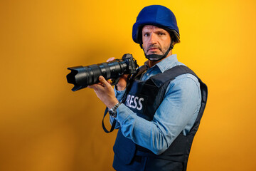 Photographer wearing a helmet and bulletproof vest that says "PRESS" is taking a photo with a camera.
