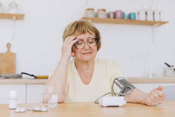 Senior woman with hypertension measuring blood pressure herself at home. Sad Elderly lady measure...
