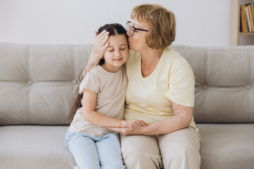 Cheerful cute granddaughter kid and happy grandma hugging with love, tenderness, affection,...